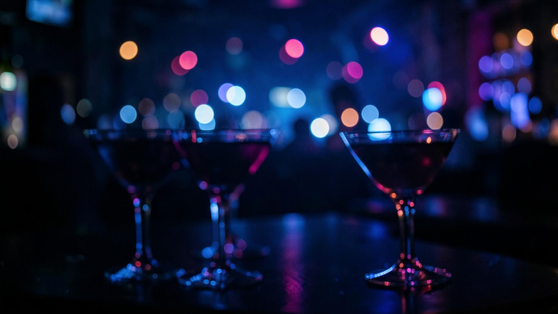 Cocktail glasses lit by colorful bokeh lights